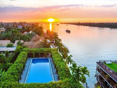 Ein atemberaubender Sonnenuntergang über dem Mekong, mit einem Pool und üppiger Vegetation im Vordergrund.