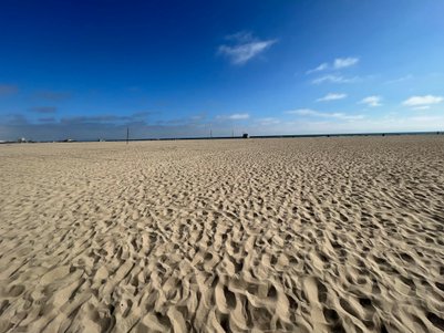 Ein weitläufiger Sandstrand erstreckt sich unter einem klaren blauen Himmel, ideal für einen entspannten Tag am Meer.