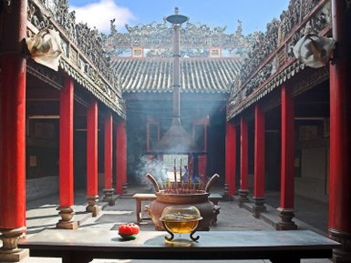 Ein traditioneller chinesischer Tempel mit roten Säulen, einem großen Räuchergefäß und aufsteigendem Rauch im Innenhof.