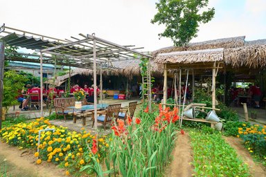 Ein einladendes Restaurant in Tra Que mit Strohdach, umgeben von bunten Blumen und Gästen, die an Tischen sitzen.
