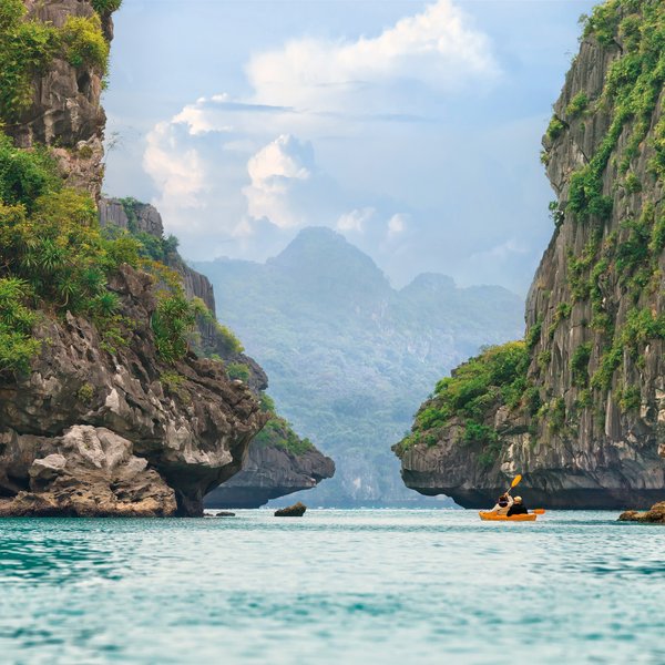 Ein Kajakfahrer paddelt durch die ruhigen Gewässer von Halong Bay, umgeben von beeindruckenden Felsen und üppiger Vegetation.