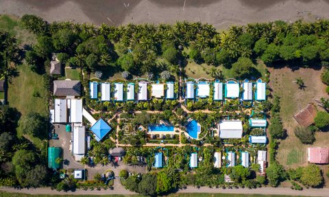 Eine Luftaufnahme eines tropischen Hotels mit blauen Dächern, umgeben von üppigem Grün und einem Pool in der Mitte.