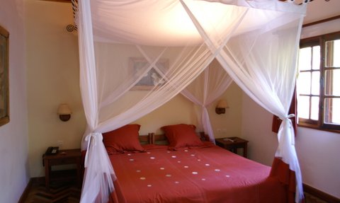 Ein gemütliches Schlafzimmer mit einem großen Bett, umgeben von einem weißen Moskitonetz und roten Kissen.