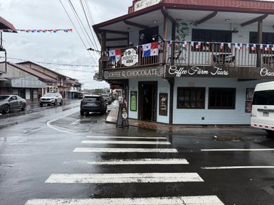 Ein geschäftiger Straßenzug mit einem Café, umgeben von feuchtem Wetter und bunten Fähnchen über der Straße.