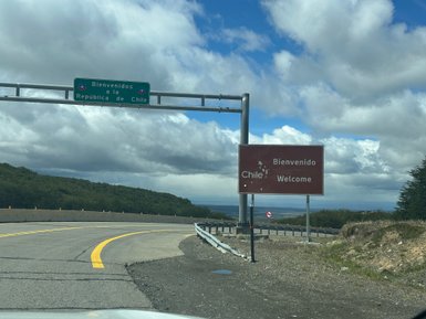 Ein Willkommensschild an der Grenze zu Chile, umgeben von grünen Hügeln und einem bewölkten Himmel.
