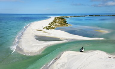 Eine malerische Küstenlandschaft mit feinem weißen Sand, klarem Wasser und einer kleinen Bootsanlegestelle im Vordergrund.