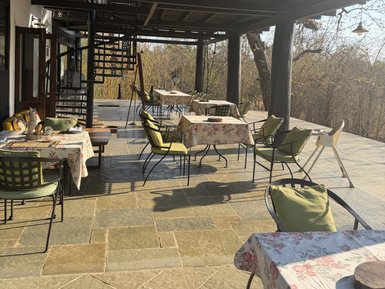 Eine einladende Terrasse mit mehreren Tischen, dekoriert mit blumigen Tischdecken, und einem Blick auf die Natur im Hintergrund.
