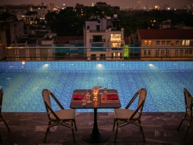 Ein romantischer Tisch für zwei mit Kerzenlicht, direkt am Rand eines glitzernden Pools in einer städtischen Umgebung.