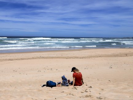 Kind sitzt mit Mutter im Sand und schaut aufs Meer – Garden Route Familienreise