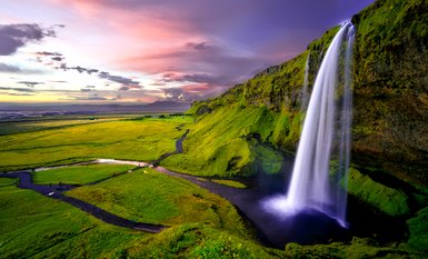 Ein majestätischer Wasserfall stürzt über grüne Klippen, während der Himmel in sanften Pastellfarben leuchtet.