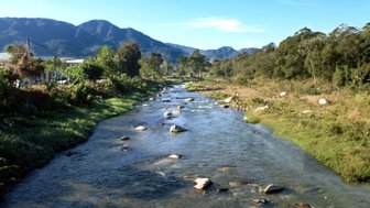 Ein klarer Fluss schlängelt sich durch eine grüne Landschaft, umgeben von Bergen und üppiger Vegetation.