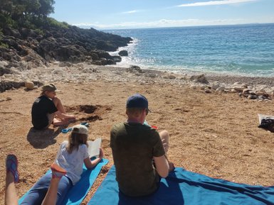 Eine Familie genießt einen sonnigen Tag am Strand, während das Kind im Sand spielt und die Erwachsenen entspannen.