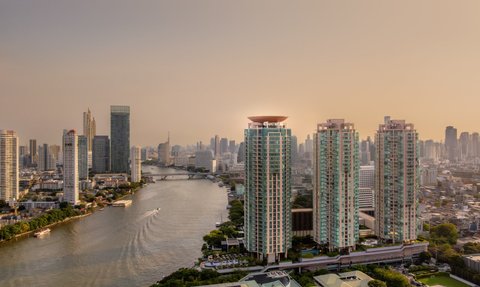 Die Skyline von Bangkok bei Sonnenuntergang, mit modernen Hochhäusern und dem ruhigen Chao Phraya Fluss im Vordergrund.