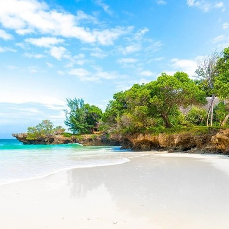 Ein ruhiger Strand mit feinem, weißem Sand und klarem, türkisfarbenem Wasser, umgeben von üppigem Grün und Felsen.