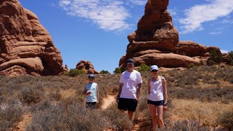 Eine Familie steht in der Wüste von Moab, umgeben von beeindruckenden roten Felsen und strahlend blauem Himmel.