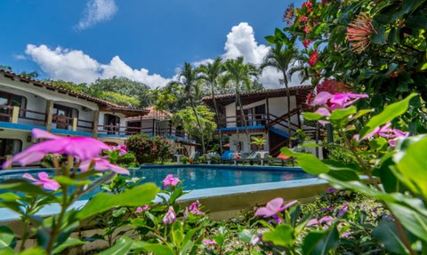 Ein einladender Außenbereich mit einem blauen Pool, umgeben von bunten Blumen und tropischen Pflanzen unter einem strahlend blauen Himmel.