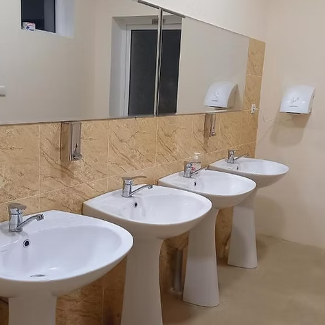 Ein modernes Badezimmer mit drei weißen Waschbecken und einem großen Spiegel an der Wand, umgeben von beige Fliesen.