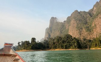 Ein Longtailboot gleitet über das ruhige Wasser, umgeben von majestätischen Bergen und üppigem Grün im Khao Sok Nationalpark.