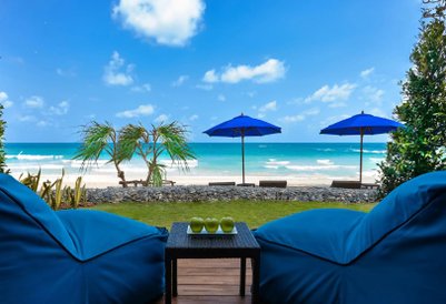 Blick auf einen Strand mit blauen Sonnenschirmen, grünen Äpfeln auf einem Tisch und gemütlichen blauen Sitzsäcken im Vordergrund.