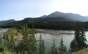 Ein malerischer Blick auf einen ruhigen Fluss, umgeben von dichten Wäldern und majestätischen Bergen im Hintergrund.