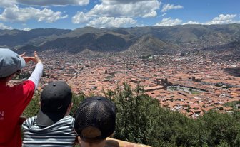 Eine Person zeigt auf die Stadt Cusco, während zwei Kinder fasziniert auf die Aussicht blicken, umgeben von Bergen.