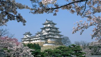 Das majestätische Himeji-Schloss erhebt sich über blühende Kirschbäume und strahlt im klaren blauen Himmel.
