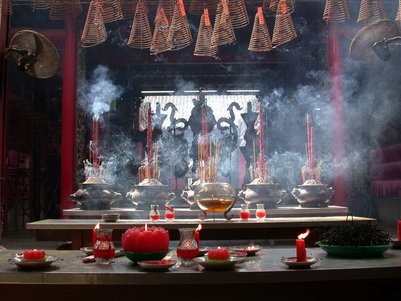 Ein geschmückter Altar mit Räucherstäbchen und Kerzen, umgeben von Rauch und einer spirituellen Atmosphäre.