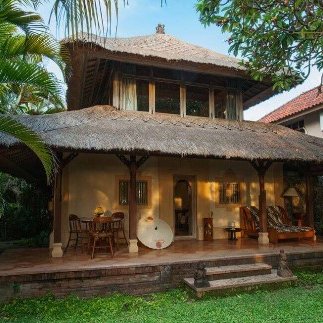 Ein traditionelles balinesisches Haus mit Strohdach, umgeben von üppigem Grün und einem einladenden Außenbereich.