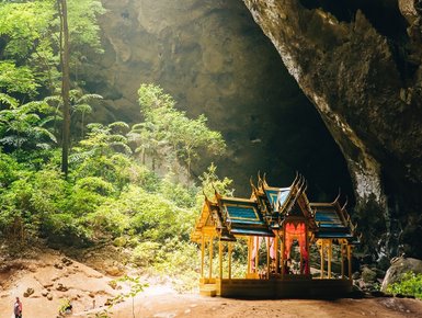 Sonnenstrahlen fallen durch die Öffnung der Phraya Nakhon Höhle auf die umliegenden Bäume - Thailand Familienreise