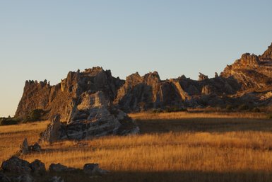 Die goldenen Gräser der Savanne kontrastieren mit den schroffen Felsen im Hintergrund, während die Sonne untergeht.