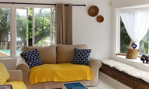 Ein gemütliches Wohnzimmer mit einem beigen Sofa, bunten Kissen und einem gelben Überwurf, das einladend wirkt.