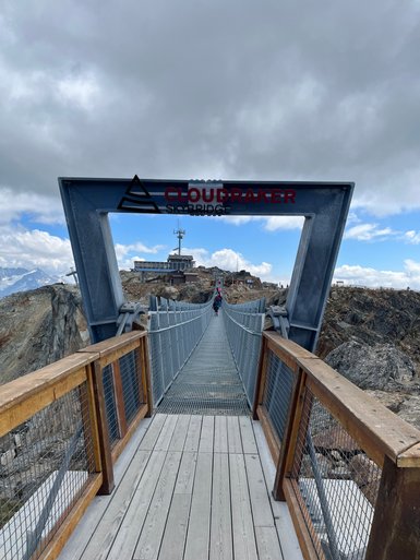 Eine beeindruckende Hängebrücke mit dem Namen Cloudraker Skybridge, die über eine felsige Landschaft führt.