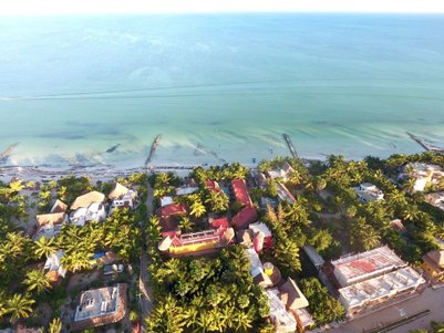 Ein atemberaubender Blick auf ein tropisches Resort mit Palmen und bunten Gebäuden, die sich entlang eines ruhigen Strandes erstrecken.