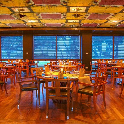 Ein elegantes Restaurant mit Holztischen und Stühlen, beleuchtet von sanften Lichtern, bietet eine einladende Atmosphäre.