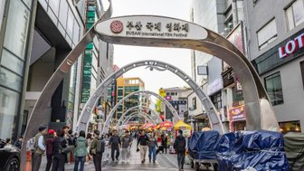 Eine belebte Straße während des Busan International Film Festivals, mit Menschen, die sich unter den geschwungenen Bögen bewegen.