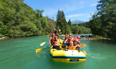 Eine Gruppe von Menschen paddelt fröhlich in einem gelben Raftingboot auf einem klaren, blauen Fluss, umgeben von üppigem Grün.