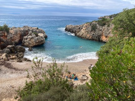 Eine ruhige Bucht mit klarem, türkisfarbenem Wasser, umgeben von Felsen und üppigem Grün, lädt zum Entspannen ein.