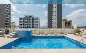 Ein glitzernder Pool auf einer Dachterrasse, umgeben von modernen Gebäuden und einem klaren blauen Himmel.