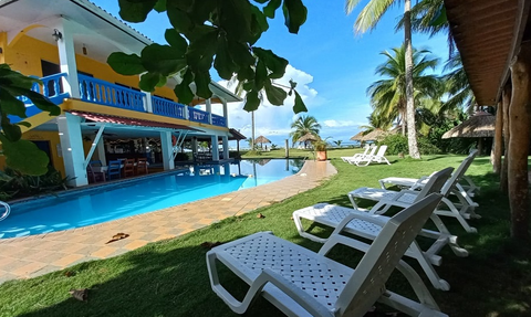 Ein einladender Poolbereich mit Liegen, umgeben von Palmen und einem farbenfrohen Gebäude im Hintergrund.