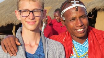 Junge begegnet einem Massai bei einem Dorfausflug – Tansania Familienreise