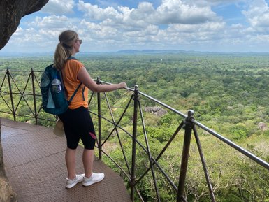 Frau blickt vom Sigiriya-Felsen auf die grüne Landschaft und den weiten Horizont – Sri Lanka Familienreise