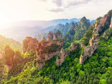 Eine atemberaubende Aussicht auf grüne Berge, die in der Morgensonne leuchten, mit schroffen Felsen und üppiger Vegetation.