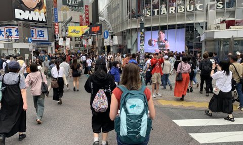 Eine belebte Straße in Shibuya, Tokio, mit vielen Fußgängern und einem großen Starbucks-Schild im Hintergrund.