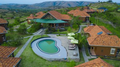 Eine Luftaufnahme des Kigarama Lodges zeigt ein Schwimmbad in Herzform, umgeben von grünen Wiesen und rustikalen Hütten.