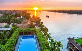 Ein atemberaubender Sonnenuntergang über dem Mekong, mit einem Pool und üppiger Vegetation im Vordergrund.