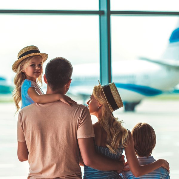 Eine Familie steht am Flughafen und beobachtet ein Flugzeug, während das kleine Mädchen auf dem Arm des Vaters sitzt.