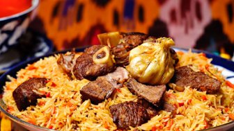 Ein Teller mit duftendem Plov, der mit zartem Fleisch und aromatischem Reis garniert ist, vor einem bunten Hintergrund.