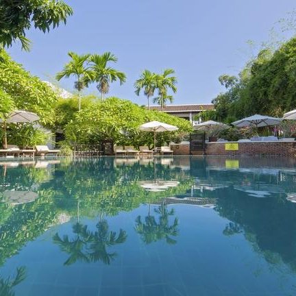 Ein ruhiger Pool umgeben von üppigem Grün und Sonnenschirmen, ideal für Entspannung und Erholung.
