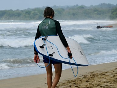 Impression eines Surfers, der mit einem Surfbrett durch den Sand am Strand von Puerto Viejo de Limon geht.