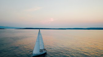 Ein Segelboot gleitet sanft über das ruhige Wasser, während der Himmel in sanften Pastellfarben leuchtet.